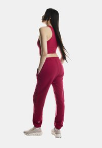 Esite heledat punane spordiriietus, mis koosneb sobivast lühikesest topsist ja vastavast pusitud vormist küljetaskutega, millele on lisatud heledates toonides tossud.