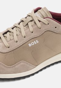 Baskets beige en daim et mesh, avec une surface texturée, une forme arrondie et le logo blanc "BOSS" sur le côté.