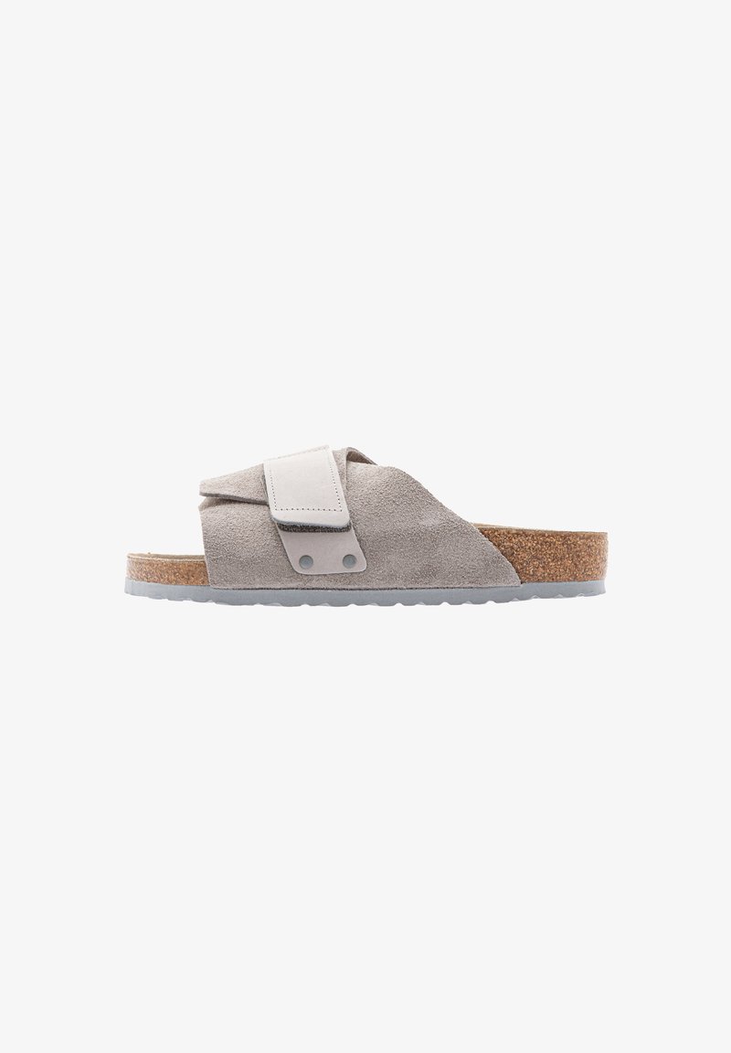 Suede slide sandal in light gray with a cork footbed. Features adjustable strap and gray rubber sole. Sleek, minimal design with soft texture.