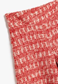 Tessuto rosso e bianco con un motivo a quadri intrecciato. Il materiale appare spesso, creando un aspetto tridimensionale. I bordi sono rifiniti in modo ordinato.