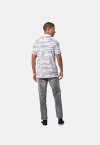 Grijze camouflage polo met korte mouwen, gecombineerd met een grijze broek. Man wordt van achteren getoond, draagt zwarte schoenen. Eenvoudig, casual ontwerp.