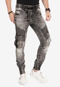 Pantalons jogger en denim gris avec des accents côtelés, multiples poches et taille élastique à cordon, présentant une coupe fuselée et des poignets élastiques.
