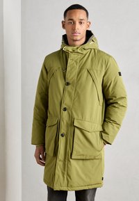 Olivovo zelený park s kapucňou, ktorý má niekoľko veľkých vreciek, gombíkové zapínanie a textúrovanú tkaninu. Slim fit a dĺžka po kolená.