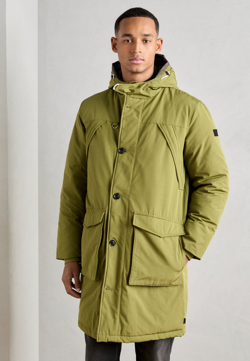 Olivovo zelený park s kapucňou, ktorý má niekoľko veľkých vreciek, gombíkové zapínanie a textúrovanú tkaninu. Slim fit a dĺžka po kolená.