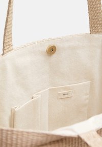 Sac fourre-tout en toile avec poignées tissées. Intérieur beige clair avec une étiquette et une poche divisée pour l'organisation. Détail de fermeture à pression en laiton.