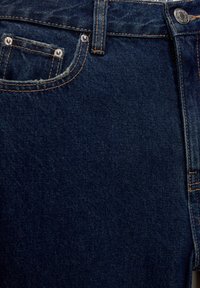 Jeans de mezclilla azul oscuro que presentan un diseño clásico de cinco bolsillos con remaches de cobre, costuras en contraste y una superficie texturizada.