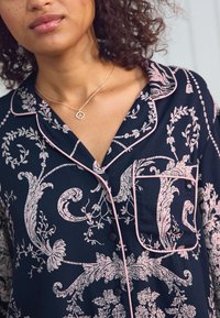 Tamsios spalvos gėlių raštas naktinės marškinėliai su rožiniais kraštais. Su mygtukų užsegimu ir krūtinės kišene. Audinys atrodo minkštas ir glotnus.