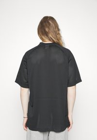 Svart mesh sportströja med korta ärmar, avslappnad passform och små utskärningar för god andningsförmåga. Enkel design utan logotyper.