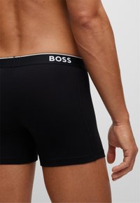 Schwarze Boxer-Shorts für Männer mit einem weichen elastischen Bund, der das "BOSS"-Logo in Weiß trägt. Der Stoff wirkt glatt und hat eine enganliegende Passform.