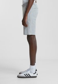 Pantalones cortos gris claro con un patrón a cuadros, diseño ajustado, bolsillos laterales y piping blanco contrastante a lo largo de las costuras.