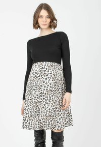 Schwarzes, geripptes Langarmoberteil kombiniert mit einem weißen Rock mit einem schwarz-braunen Leopardenmuster. Modell trägt schwarze kniehohe Stiefel.