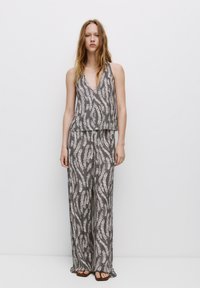 Grijs patroon twee-delige outfit met een mouwloze top met V-hals en wijde broek, beide met een gestructureerd abstract ontwerp.