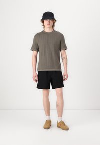 Grå ribbet T-shirt med korte ærmer, sorte shorts, beige sneakers, hvide sokker og en navy bucket hat. Simpelt design med en afslappet pasform.