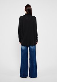 Blusa nera a maniche lunghe con un motivo testurizzato e una leggera lucentezza, abbinata a jeans in denim blu a gamba larga.