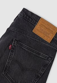 Μαύρο τζιν Levi's διπλωμένο για να φαίνεται η πίσω τσέπη και η δερμάτινη ετικέτα της μάρκας με το λογότυπο και λεπτομέρειες ραφής.