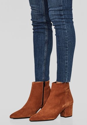 Braune Wildleder-Stiefeletten mit spitzer Zehe und Blockabsatz, ausgestattet mit einem seitlichen Reißverschluss und weicher Textur, kombiniert mit dunkelblauen Slim-Fit-Jeans.