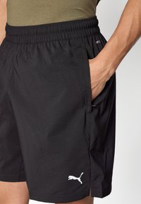 Μαύρο αθλητικό σορτς με ελαστική μέση, διαθέτει πλαϊνές τσέπες και λευκό λογότυπο Puma στο κάτω αριστερό μέρος. Λείο υφή υφάσματος.