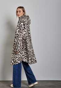 Abrigo con capucha de estampado de leopardo y corte holgado, con un lado abotonado, hecho de tela suave. Combinado con pantalones de denim de pierna ancha.