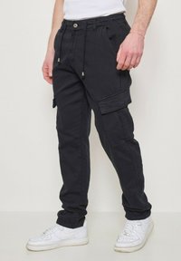 Pantalons cargo noirs avec taille élastique ajustable, poches latérales et coupe décontractée, associés à des baskets blanches.