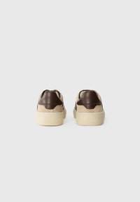 Baskets avec une tige en daim beige, des accents en cuir marron et une semelle en caoutchouc crème texturée. Design classique avec des détails minimalistes.