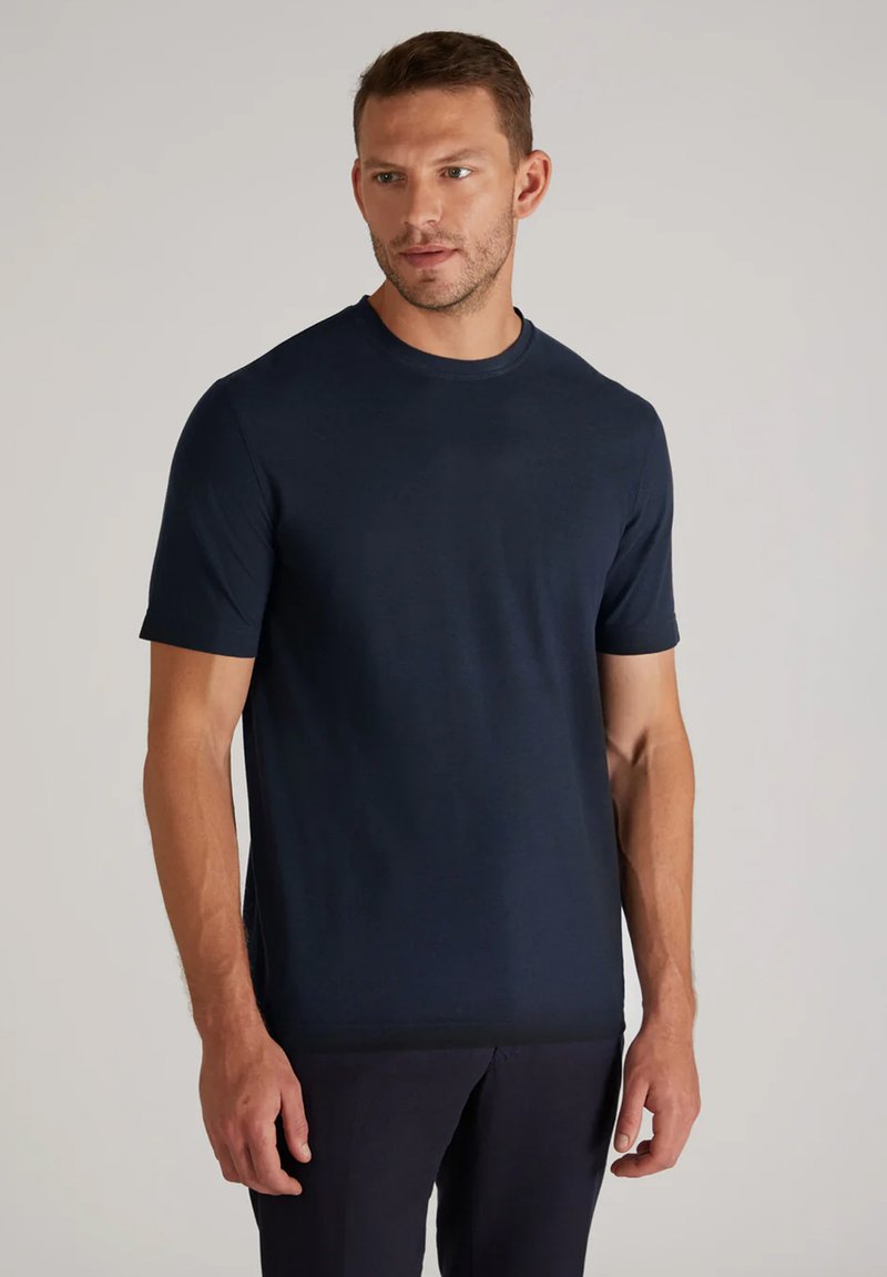 T-shirt à manches courtes bleu marine en tissu lisse, avec un col rond et une coupe décontractée, porté avec un pantalon sombre.