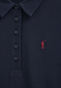 Navyblauw poloshirt met vier donkere knopen en een klein rood geborduurd figuurtje van een persoon die een polo mallet vasthoudt op de borst.