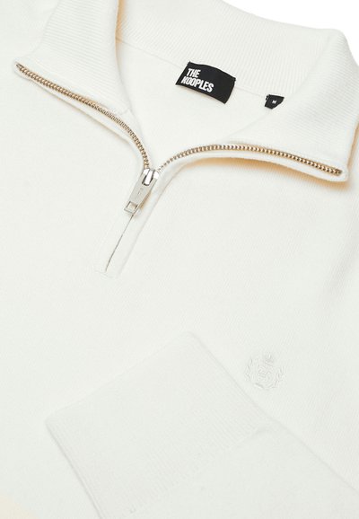 Weißer Reißverschluss-Pullover aus geripptem Stoff mit einem halben Reißverschluss an der Vorderseite, Stehkragen und dezentem, gesticktem Logo auf der linken Seite.
