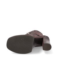 Zapato de tacón de cuero marrón con suela de goma negra texturizada, que presenta un cierre lateral con cremallera y un diseño de tacón curvado.