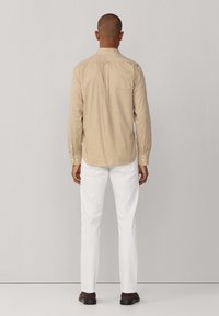 Camisa de cuadros de manga larga en beige y amarillo, mezcla de algodón, con cuello abotonado y pliegue en la espalda, combinada con pantalones blancos ajustados.