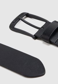 Μαύρη δερμάτινη ζώνη με ματ φινίρισμα, που διαθέτει ορθογώνια μεταλλική αγκράφα. Το λουρί είναι λείο με στρογγυλεμένη άκρη και ελάχιστες λεπτομέρειες.