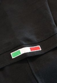 Juodas drabužis, turintis mezginį tekstūrą, su išsiuvinėta Italijos vėliavos akcentu žalios, baltos ir raudonos spalvų apačioje.