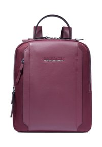 Rucksack aus kastanienbraunem Leder mit klarer Form, zwei Griffen und Reißverschluss. Verfügt über ein dezentes Logo und eine Seitentasche. Glatte Textur.