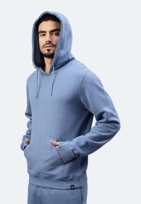 Felpa sportiva blu realizzata in tessuto morbido, con tasca frontale, cappuccio con cordini, polsini a costina e un piccolo logo etichetta sull'orlo.