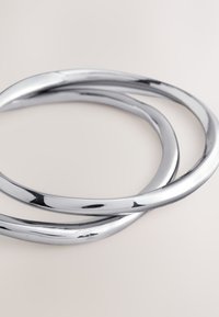 Drei ineinandergreifende Armreifen aus poliertem Silbermetall, die glatte, geschwungene Formen mit reflektierenden Oberflächen und moderater Dicke aufweisen.