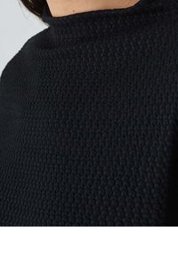 Tissu noir texturé avec un motif en relief. Gros plan sur un design à col haut, mettant en valeur des détails complexes et une surface lisse.