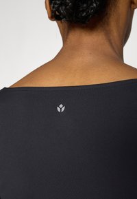 Čierna dlhá košeľa s výstrihom do pása vzadu a malým svetlosivým logom na hornej časti chrbta pri krku. Mäkká tkanina.