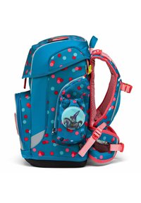 Sac à dos bleu avec des pois rouges et teal, plusieurs poches zippées, bretelles rembourrées en mesh et un badge rond affichant un design de personnage.