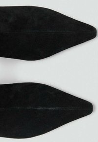 Chaussures en daim noir à bout pointu avec une texture lisse et un détail de couture le long du centre, présentant un design minimaliste.