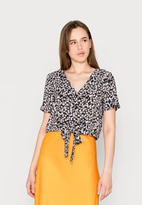 Blusa preta de flores com mangas curtas, decote em V e laço na frente, combinada com uma saia de cetim laranja brilhante. Apresenta padrões de flores brancas e rosas.