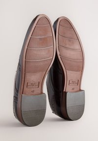 Chaussures en cuir marron texturé avec une semelle en caoutchouc grise lisse. Détails brogue le long des bords, taille 42 indiquée sur la semelle intérieure.