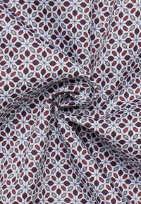 Tessuto in cotone con un motivo geometrico di forme rosse, verdi e nere su uno sfondo bianco con una superficie testurizzata.