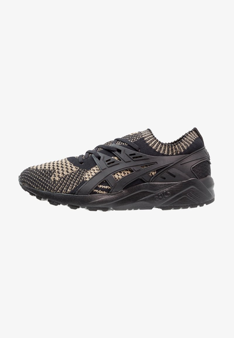 Chaussure de course tricotée noire et beige avec cage de soutien à lacets noire et semelle noire épaisse, vue de côté gauche.