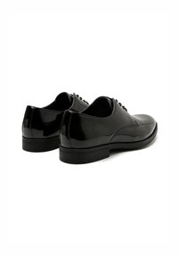 Zapatos de charol negro con un acabado suave, punta redondeada y suela de goma plana. Presentan seis ojetes para cordones y mínimos detalles de costura.