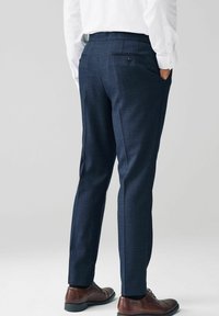 Pantalones entallados azul marino con un tejido texturizado, diseño de ajuste slim, dos bolsillos traseros y zapatos de cuero marrón visibles en la parte inferior.
