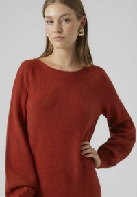 Maglione rosso a maglia con scollatura rotonda e maniche lunghe, dal taglio morbido e rilassato. La texture è soffice e leggermente pelosa.