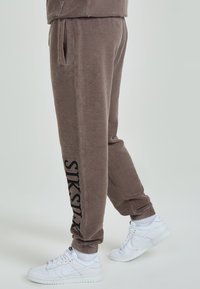Bruna fleece-joggers med sidofickor har en svart logotypdetalj på vänster ben. Kombinationen med vita sneakers och ribbade mudd är perfekt.