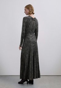 Vestido de manga larga, con rayas negras y doradas, cuerpo ajustado, falda acampanada, escote en V y tejido texturizado. Tacones negros completan el conjunto.