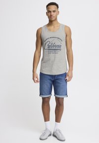 Camiseta sin mangas gris con estampado gráfico en azul marino, combinada con pantalones cortos de mezclilla doblados en el dobladillo. La modelo lleva zapatillas grises y calcetines blancos.