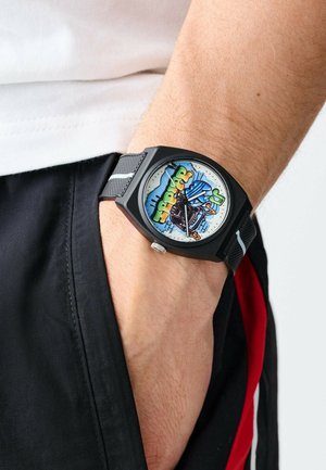 Montre noire avec un boîtier hexagonal, cadran graphique coloré présentant des motifs bleus, verts et rouges, et un bracelet texturé avec des accents gris.