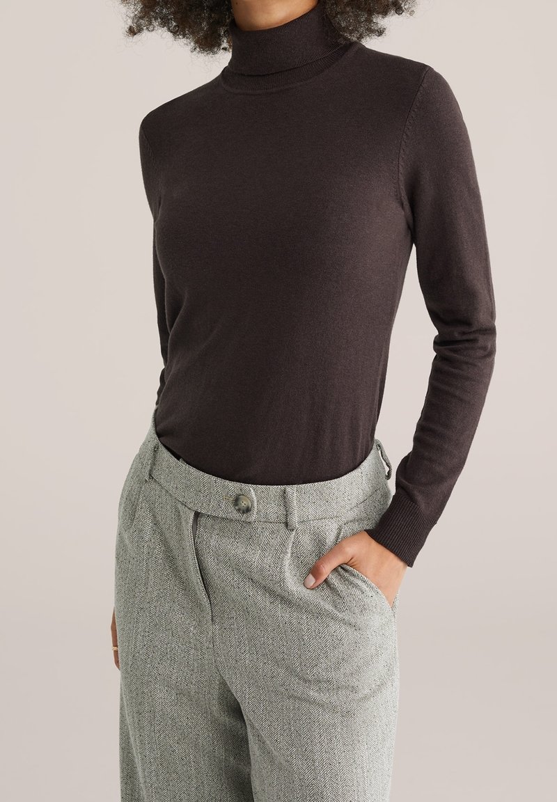 Pull à col roulé à manches longues de couleur marron foncé, associé à un pantalon gris clair à motif pied-de-poule. Texture lisse et coupe ajustée.